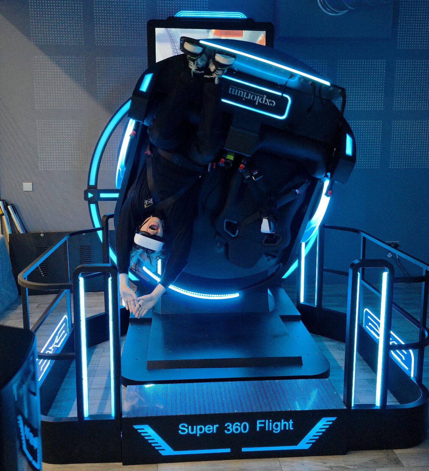 Person enjoying virtual reality simulator ride, upside-down in Super 360 Flight machine, with vibrant blue lights.