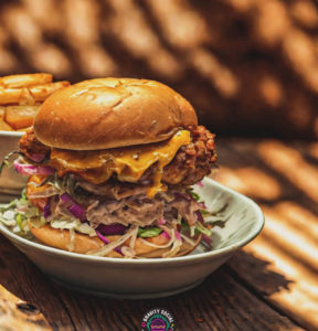 Delicious crispy chicken burger with cheese, fresh veggies, and side of fries on a rustic wooden table.