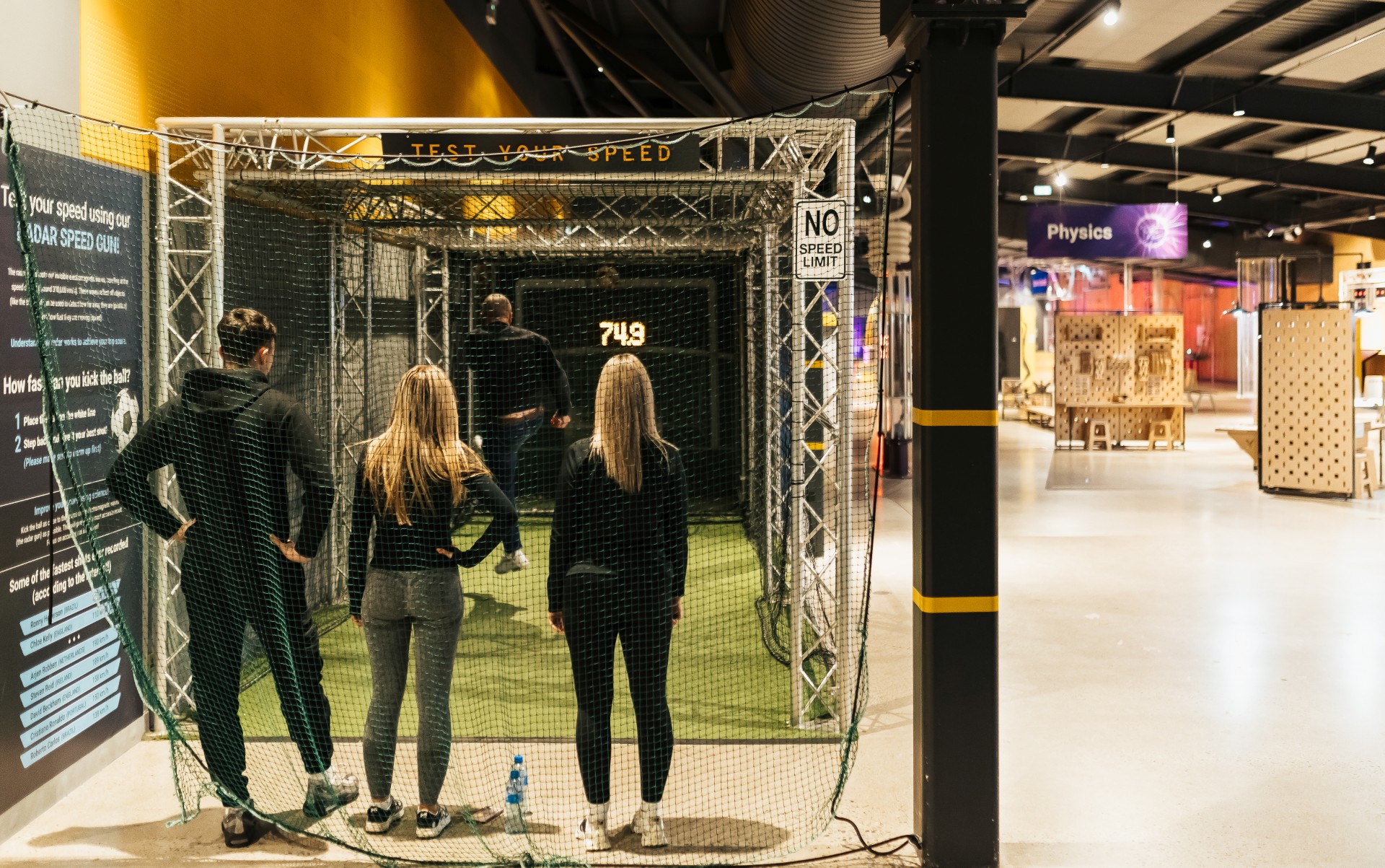People testing their speed in an interactive indoor sports exhibit with a speed radar display and no speed limit sign.