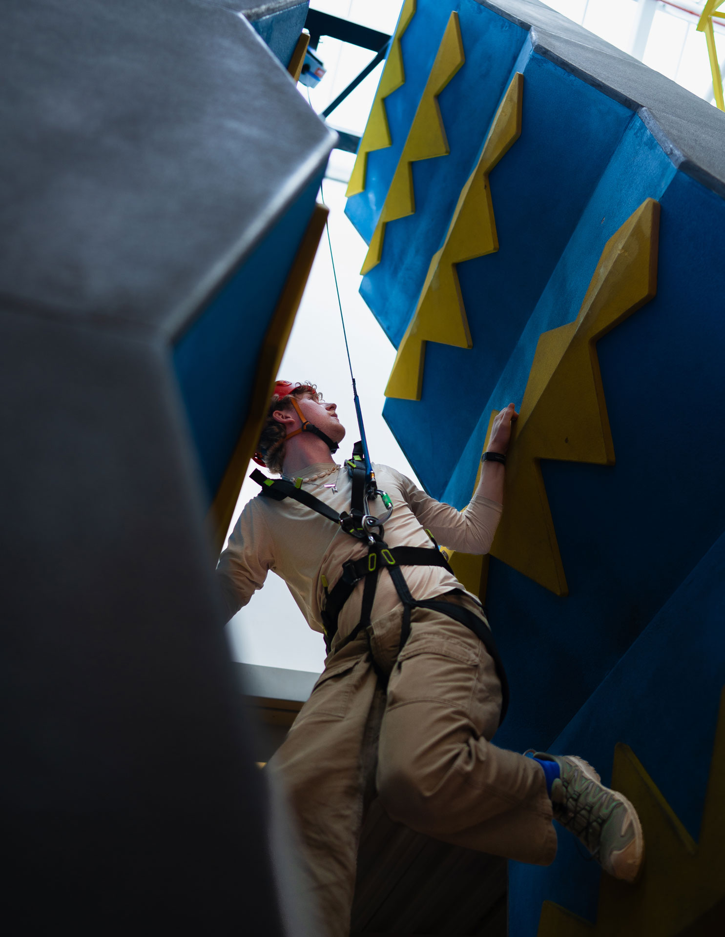 Person bouldering indoors with safety gear on a colorful climbing wall.