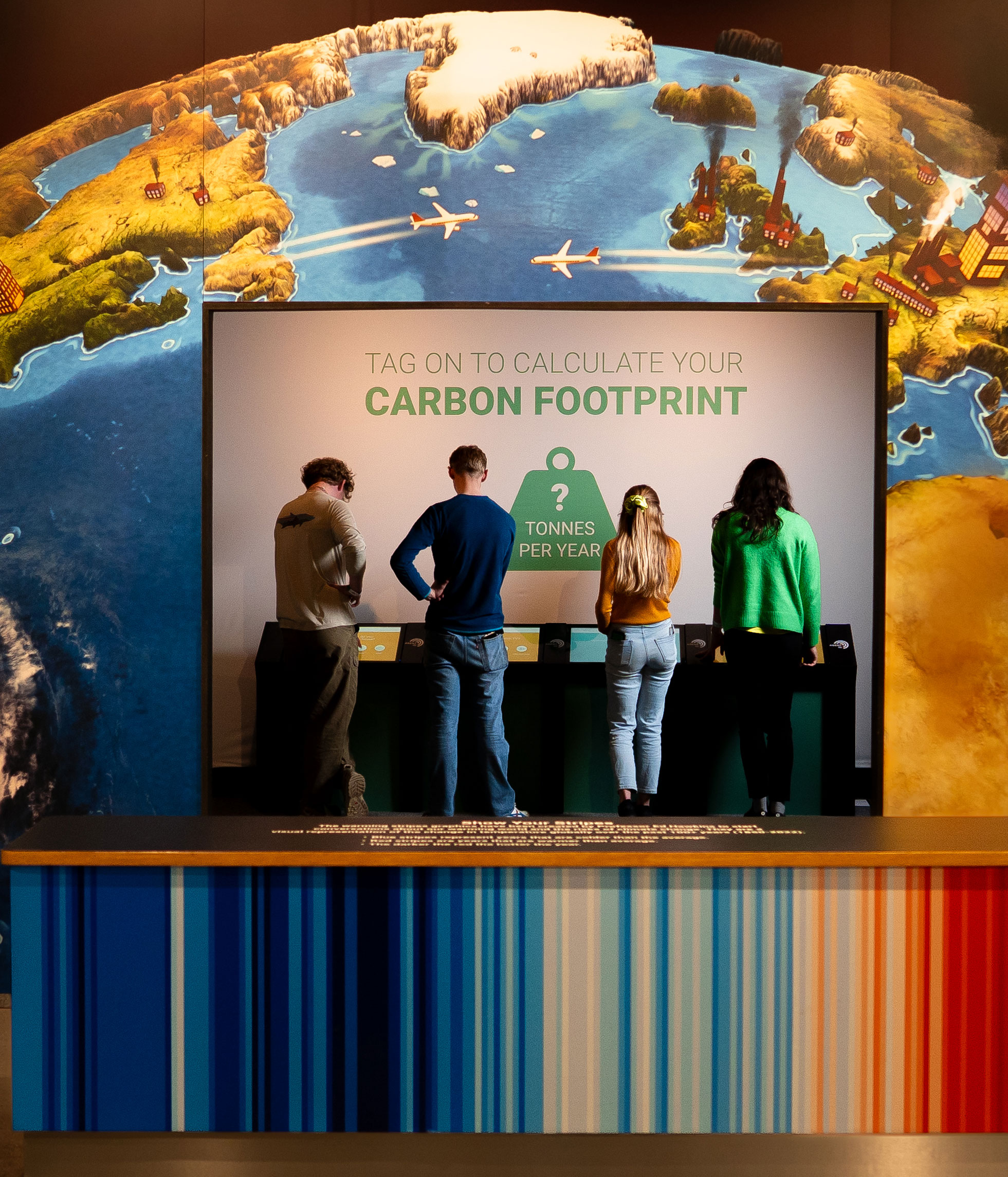 Visitors using a carbon footprint calculator exhibit beneath a world map illustration.